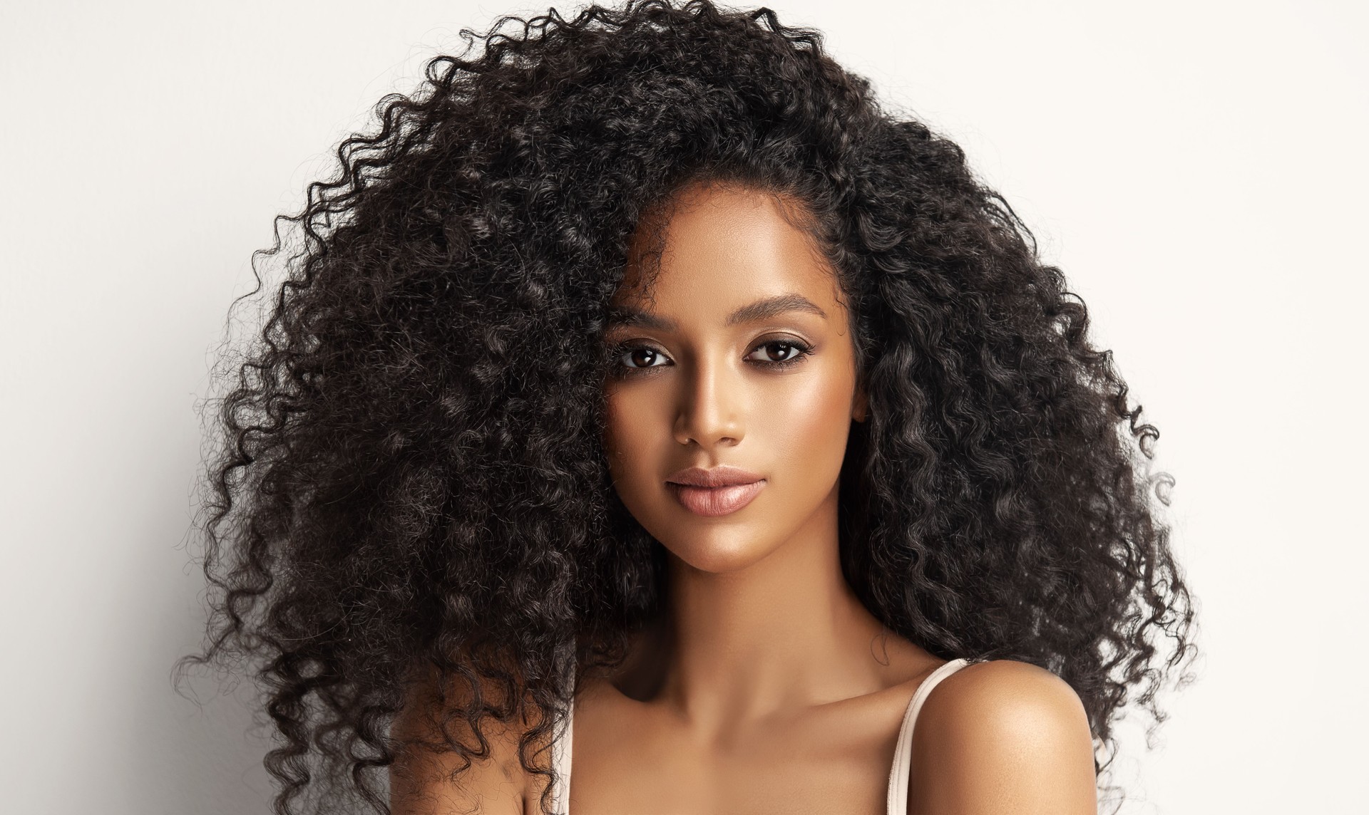 Model with vibrant melanin-rich skin tone is demonstrating long dense curly hair. Natural Afro hair. Afro beauty.